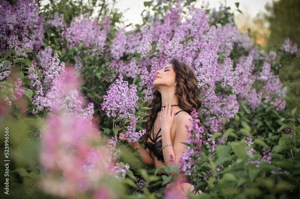 a beautiful girl with makeup and hair styling in underwear stands in a garden with lilacs on a summer evening a beautiful girl with makeup and hair styling in underwear stands in a garden with lilacs on a summer evening