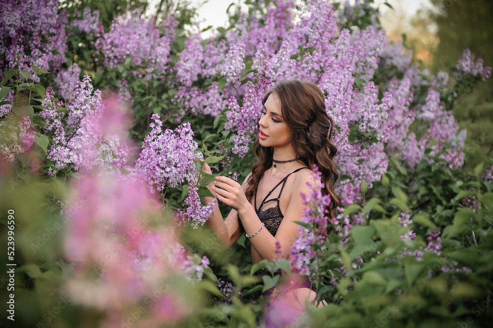 a beautiful girl with makeup and hair styling in underwear stands in a garden with lilacs on a summer evening a beautiful girl with makeup and hair styling in underwear stands in a garden with lilacs on a summer evening