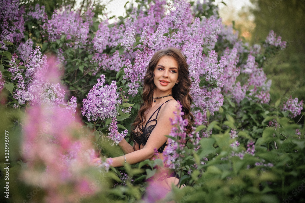 a beautiful girl with makeup and hair styling in underwear stands in a garden with lilacs on a summer evening a beautiful girl with makeup and hair styling in underwear stands in a garden with lilacs on a summer evening