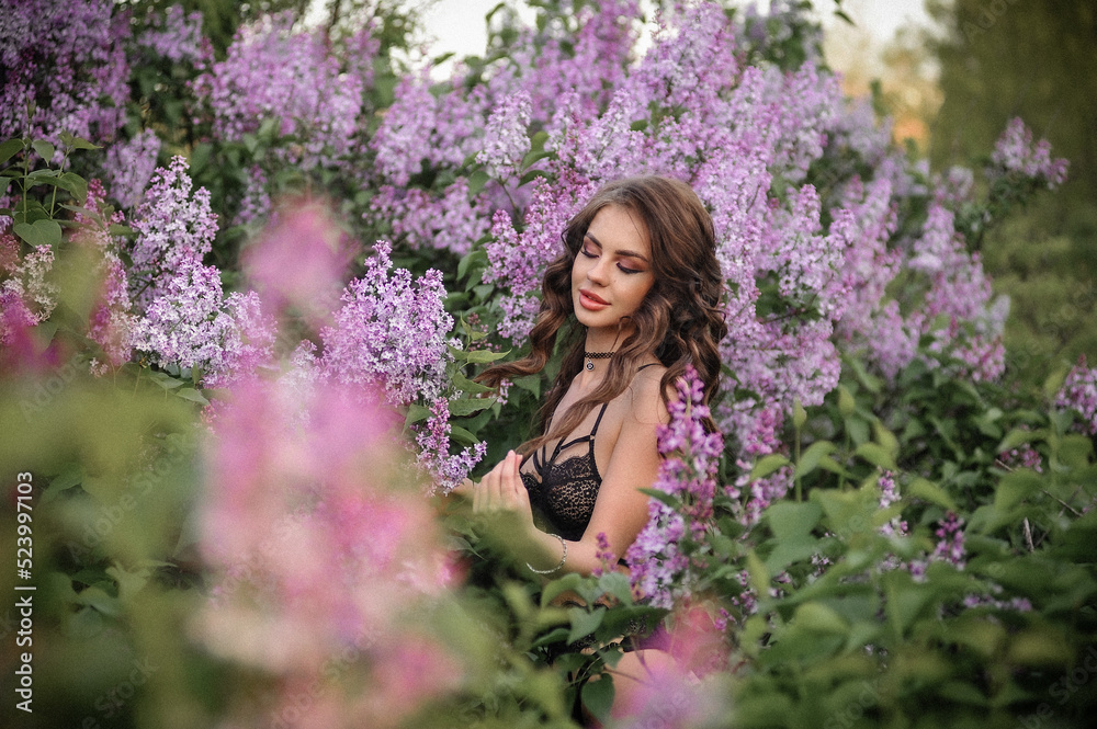a beautiful girl with makeup and hair styling in underwear stands in a garden with lilacs on a summer evening a beautiful girl with makeup and hair styling in underwear stands in a garden with lilacs on a summer evening