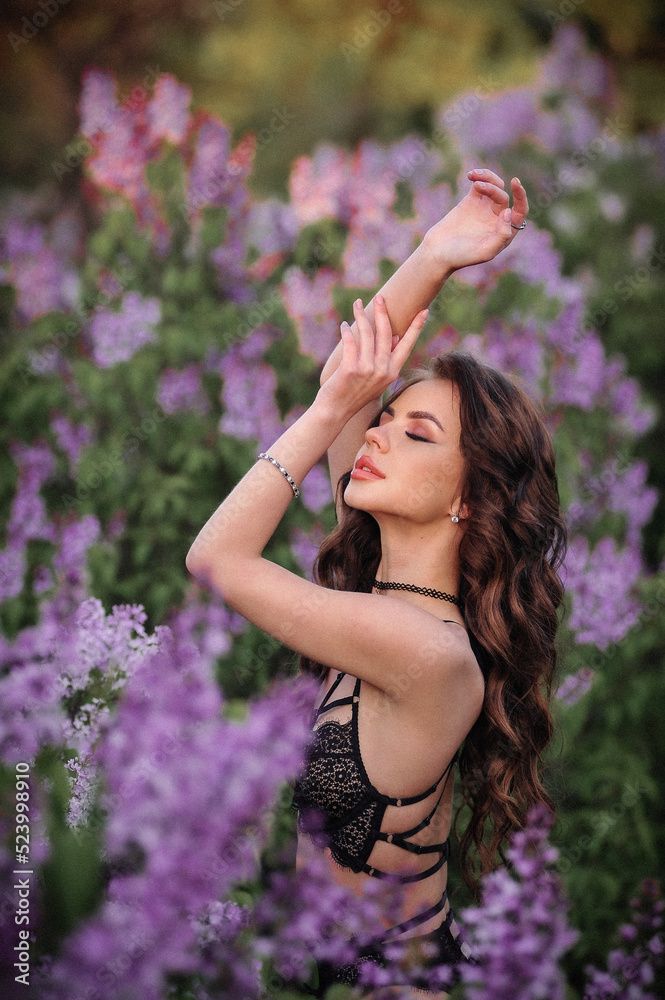 a beautiful girl with makeup and hair styling in underwear stands in a garden with lilacs on a summer evening a beautiful girl with makeup and hair styling in underwear stands in a garden with lilacs on a summer evening
