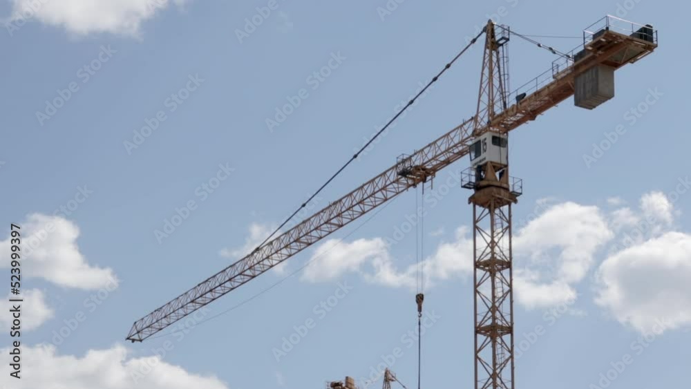 A working construction tower crane against a cloudy sky on a sunny day. The concept of urban development and construction. Industrial background. Crane engineering, construction industry tool. A working construction tower crane against a cloudy sky on a sunny day. The concept of urban development and construction. Industrial background. Crane engineering, construction industry tool.