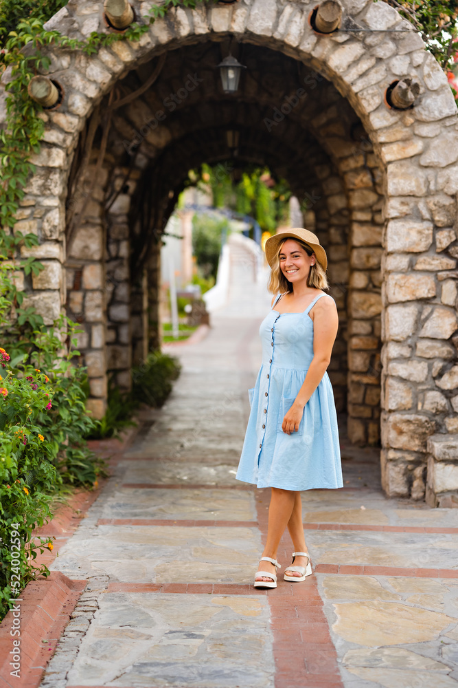 Portrait of a pretty young woman in a blue dress and straw hat. Summer vacation.Background of an old historical stone arch building