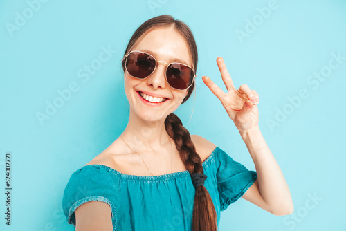 Young beautiful smiling female in trendy summer  overalls. Sexy carefree woman with tail hairstyle posing near wall in studio. Positive model having fun. Cheerful and happy. Taking selfie Pov photos