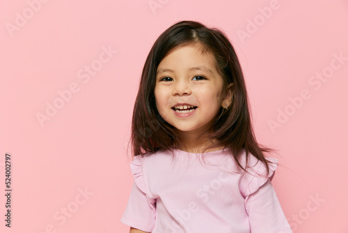 a little beautiful girl of preschool age stands on a pink background in a pink T-shirt with her hair down, looks at camera with incomprehension  photo