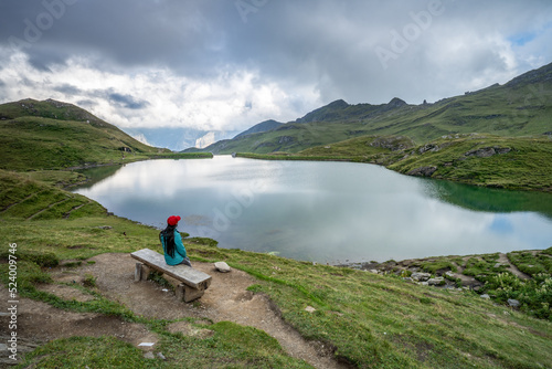Young woman sitting on a wooden bench in front of Bachalpsee, Bernese Oberland, Grindelwald, Switzerland