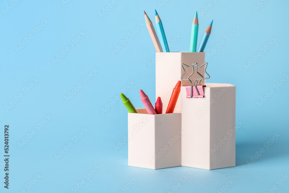 Cups with pencils, crayons and paper clip on blue background Cups with pencils, crayons and paper clip on blue background