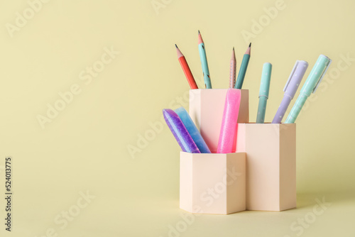 Cups with pens, pencils and glitters on beige background