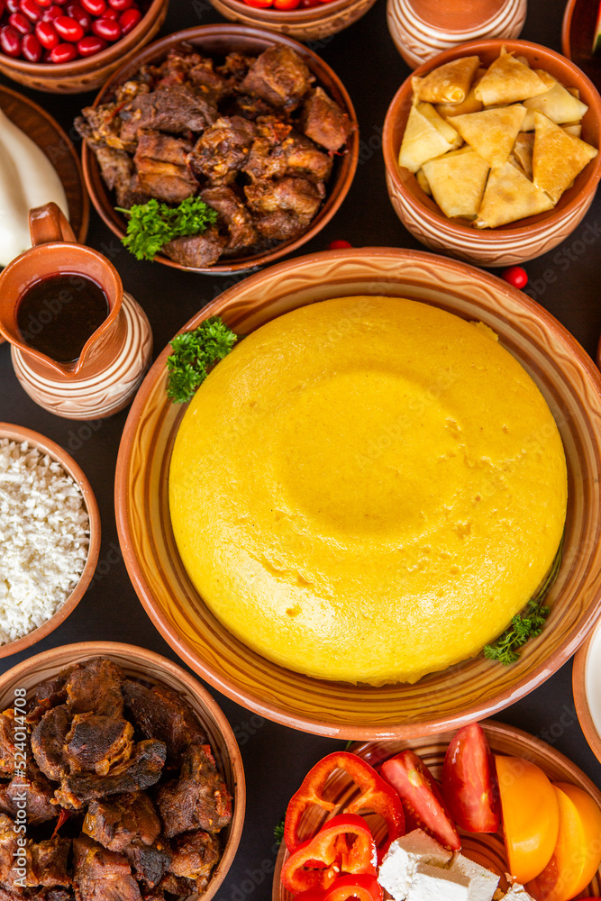 Homemade Romanian Food with polenta, meat, cheese and vegetables. Delicious corn porridge in clay dishes. Mamaliga or polenta, a traditional dish in Moldova, Hungary and Ukrainian cuisine.
