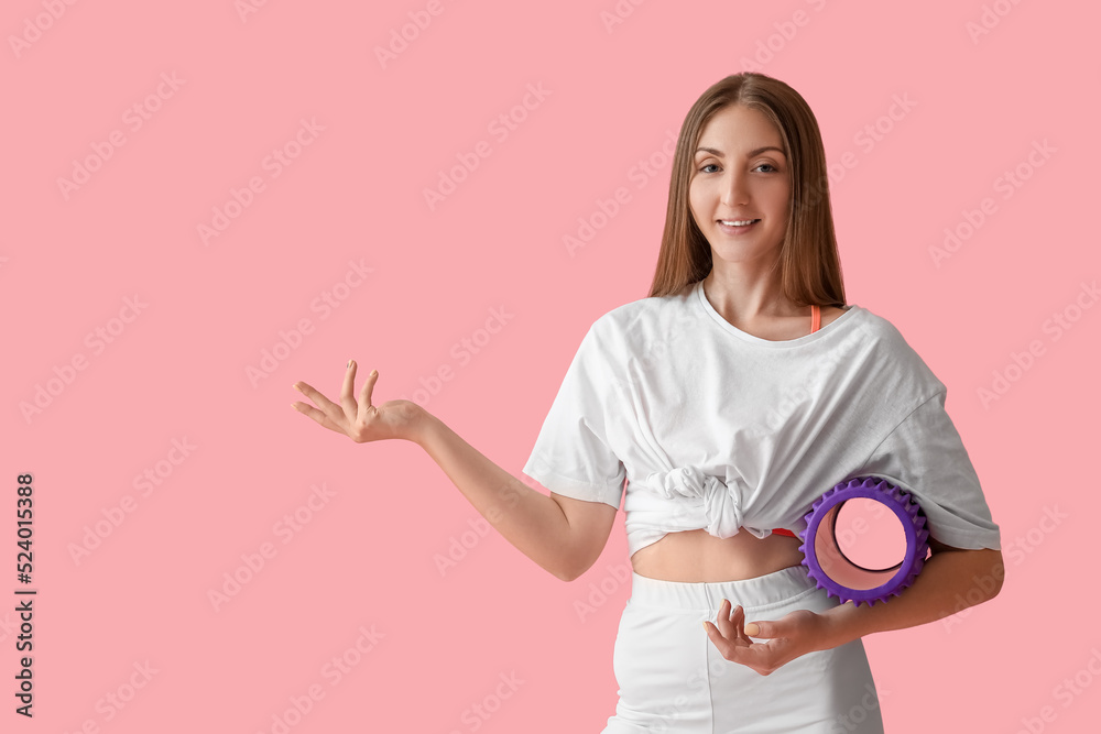 Young woman with foam roller showing something on pink background Young woman with foam roller showing something on pink background