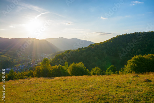 mountainous rural landscape on a sunny afternoon. forested hills and green grassy meadows in evening light. ridge in the distance. sunny weather with fluffy clouds on the bright blue sky © Pellinni