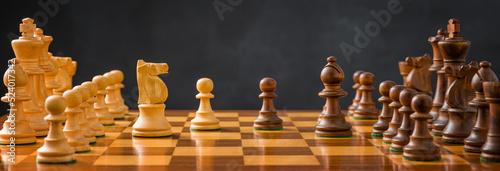 Fototapete Chess pieces on a chessboard with a dark background