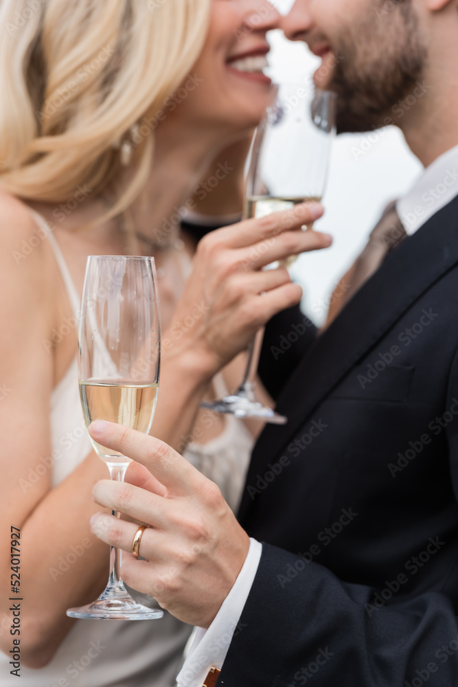 Cropped view of champagne in hand of groom kissing bride outdoors. Cropped view of champagne in hand of groom kissing bride outdoors.