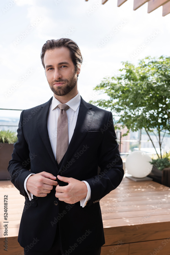 Portrait of groom looking at camera while adjusting jacket outdoors. Portrait of groom looking at camera while adjusting jacket outdoors.