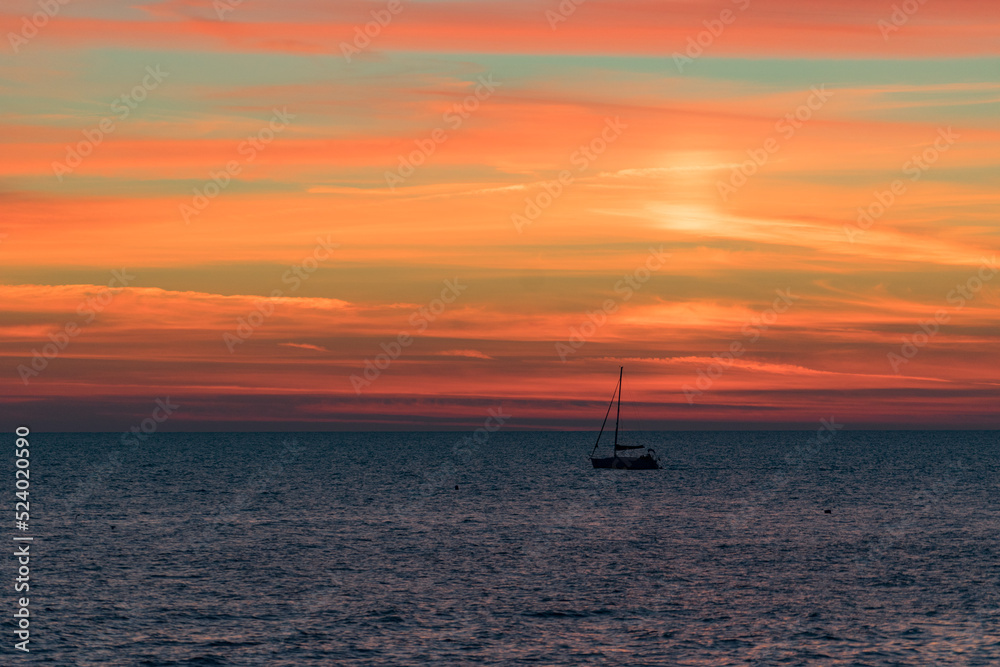 Seascape with a vibrant sunset over a calm sea and a floating boat.
