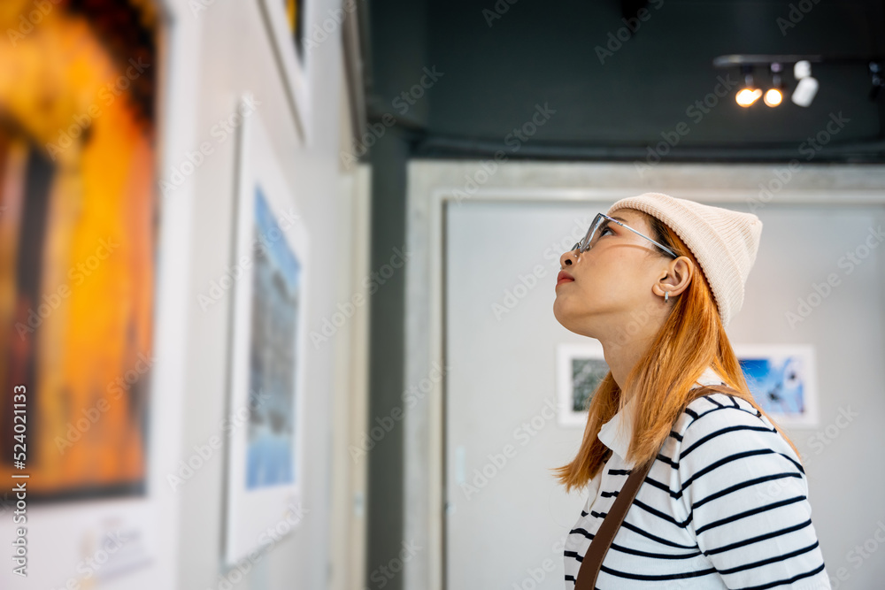 Woman standing she looking art gallery collection in front framed paintings pictures on white wall, Asian people watch at photo frame to leaning against at show exhibition artwork gallery, Side view Woman standing she looking art gallery collection in front framed paintings pictures on white wall, Asian people watch at photo frame to leaning against at show exhibition artwork gallery, Side view