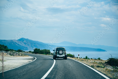 Rear view of SUV car driving on highway along the Adriatic sea with beautiful mountain view and blue clouds