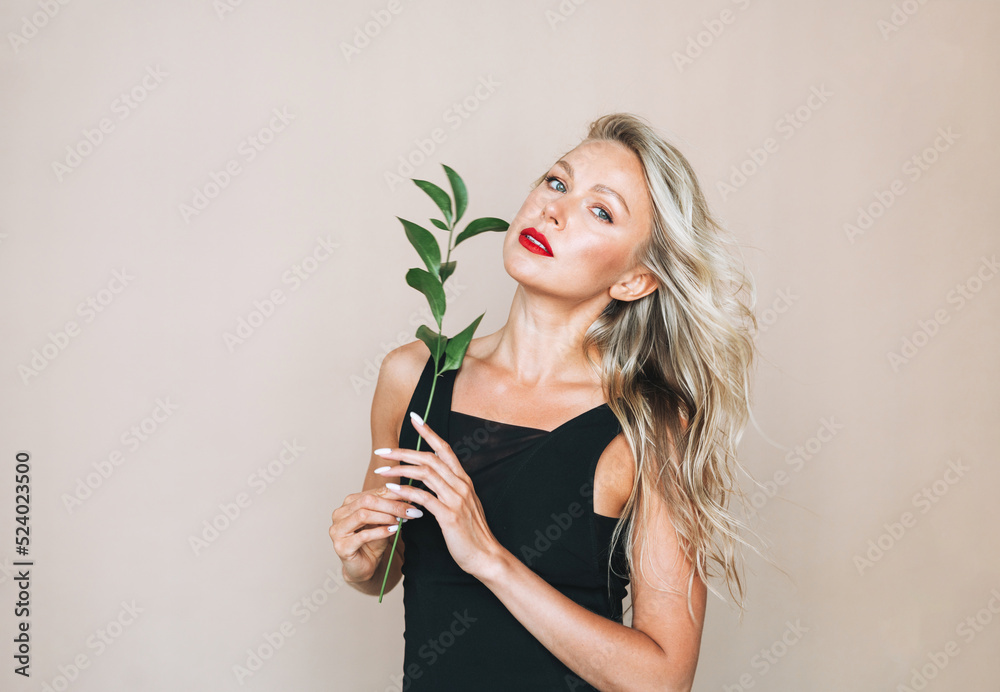 Portrait of gorgeous beautiful blonde young woman with bright makeup in evening dress with green twig on beige background Portrait of gorgeous beautiful blonde young woman with bright makeup in evening dress with green twig on beige background
