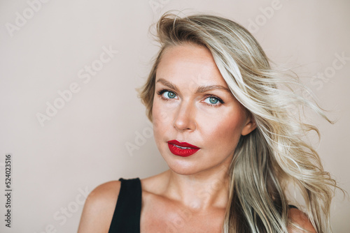 Close up portrait of beautiful blonde young woman with bright makeup in evening dress on beige background