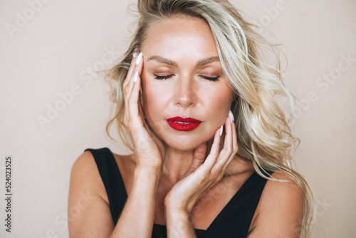 Close up portrait of beautiful blonde young woman with bright makeup and closed eyes in evening dress on beige background