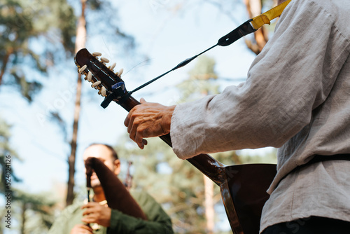 Musician playing ethnic guitar at outdoor entertainment, close-up. Musical folk group at a street festival, selective focus on the guitarist's hand