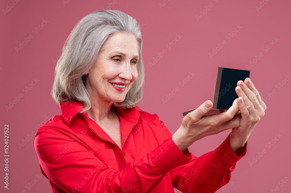 Mature woman in red doing makeup and looking contented Mature woman in red doing makeup and looking contented