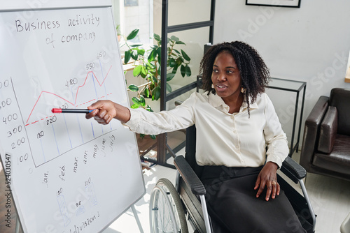 African Businesswoman with disability pointing at flipchart and presenting her business strategy at meeting at office photo