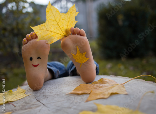 yellow autumn leaf between the toes on the bare feet of a toddler child. painted smile on the feet. indulge, positive thinking, happy childhood. Hello, Autumn. seasonal fun photo ideas photo