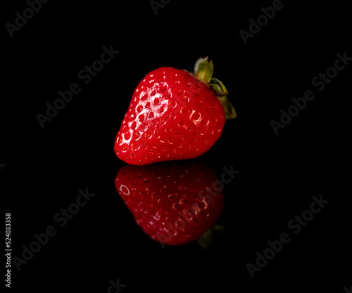 Single ripe red strawberry on a black reflective background