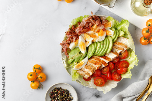 Cobb salad with grilled chicken, eggs, avocado, tomato, bacon on marble white background. Keto diet. photo