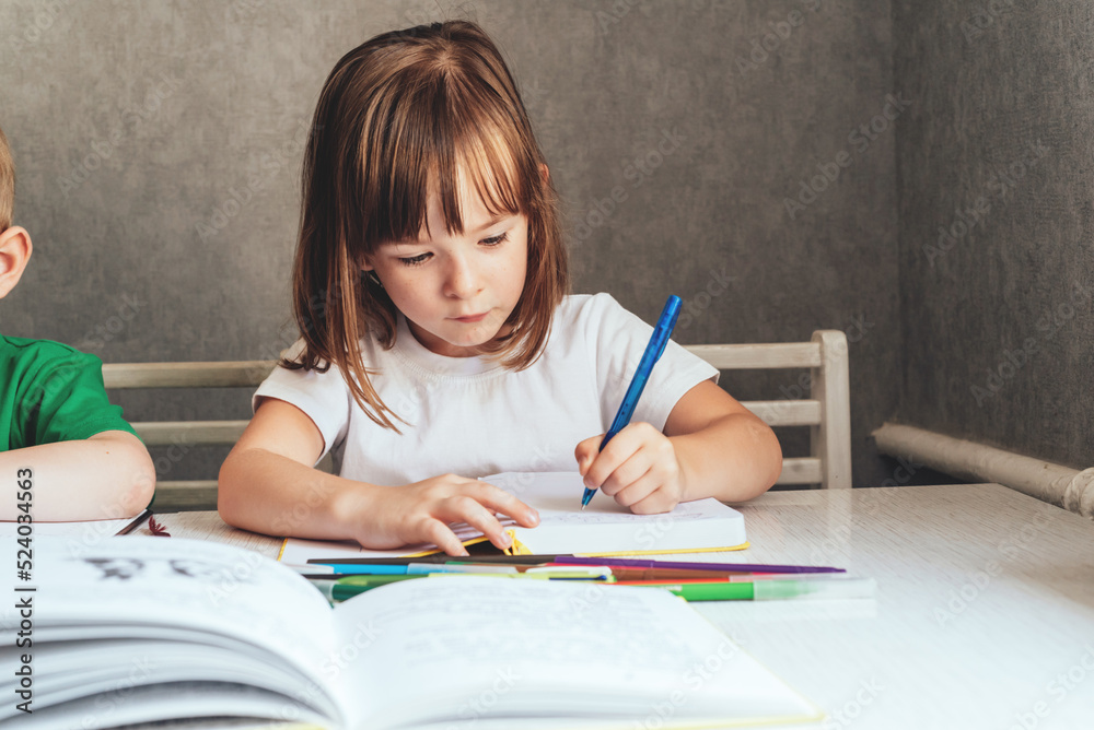 The girl sits at the table and writes with a pen in a notepad. Looks at the notebook. Home education concept The girl sits at the table and writes with a pen in a notepad. Looks at the notebook. Home education concept