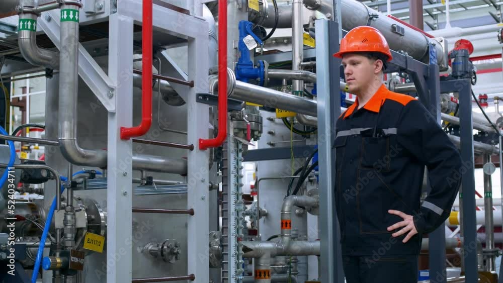 A worker in overalls and an orange work helmet at the workplace. Work in heavy industry with mechanical equipment. The operator of the compressor and pumps checks the stable operation. A worker in overalls and an orange work helmet at the workplace. Work in heavy industry with mechanical equipment. The operator of the compressor and pumps checks the stable operation.