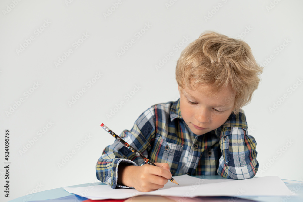 Boy with a pencil sitting at a table and writing, school education Boy with a pencil sitting at a table and writing, school education