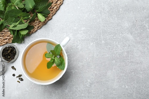 Cup of aromatic green tea with mint and dry leaves on grey table, flat lay. Space for text