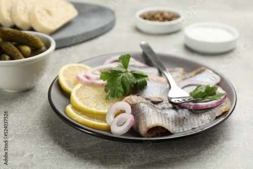 Delicious salted herring fillets served with lemon, onion rings and parsley on grey table, closeup