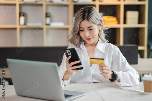 Young beautiful Asian woman smiling and happy  showing presenting credit card online shopping using with mobile phone app pay online copy space.
