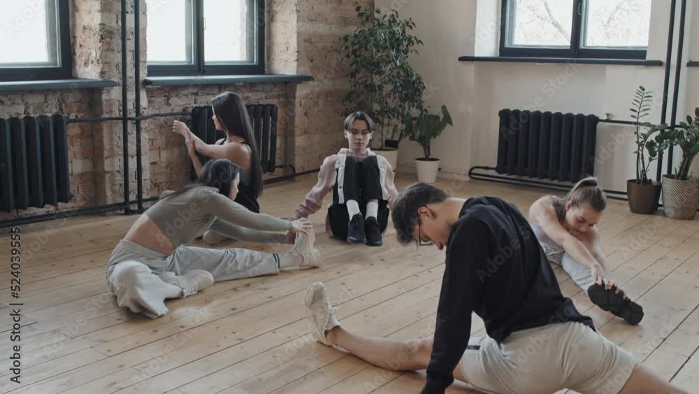 Medium long of young female and male dancers stretching together in studio in morning Medium long of young female and male dancers stretching together in studio in morning