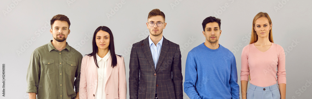 Group studio portrait of company staff. Team of 5 young business people in smart casual wear standing in row and looking at camera with serious facial expressions