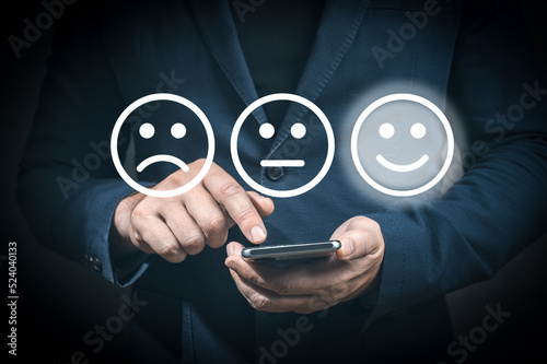 Businessman pressing excellent smiley face rating icon over dark blue background, customer service evaluation and feedback rating. costumer review concept, man using phone chooses happy smiling face photo