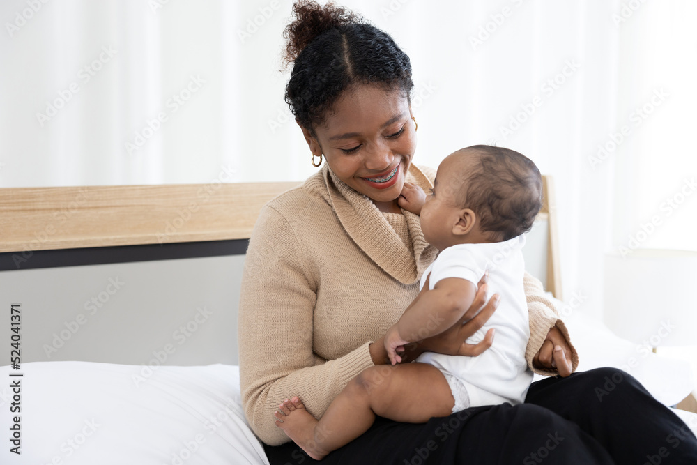 close up African young mother carrying and playing with her adorable baby on bed close up African young mother carrying and playing with her adorable baby on bed
