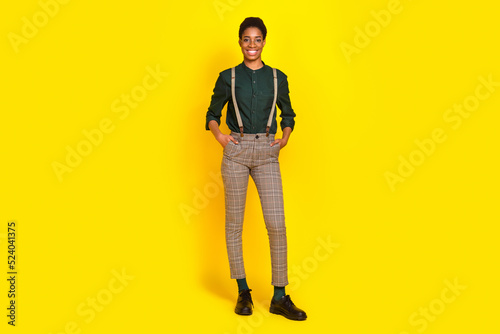 Full length body size view of attractive cheery woman holding hands in pockets posing isolated over bright yellow color background
