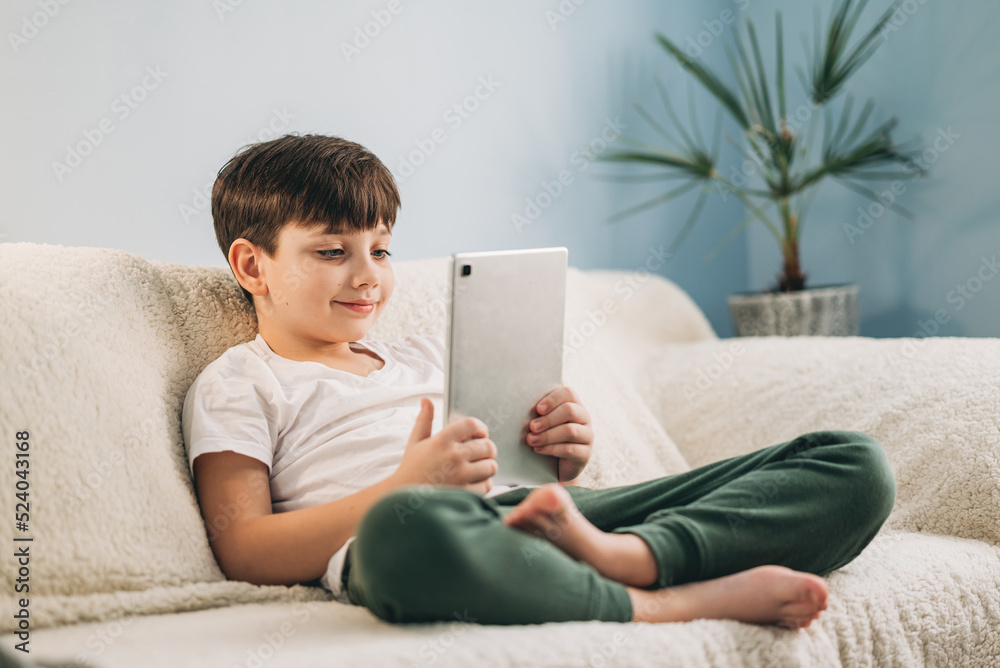 Boy playing mobile game on tablet on sofa. Preschooler playing mobile games. Kid using device for gaming. Child playing video game at home. Communication and chat device Boy playing mobile game on tablet on sofa. Preschooler playing mobile games. Kid using device for gaming. Child playing video game at home. Communication and chat device