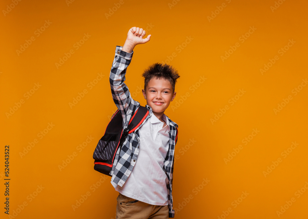 A student greets on a yellow background. portrait of a boy with a backpack and a folder. A student greets on a yellow background. portrait of a boy with a backpack and a folder.