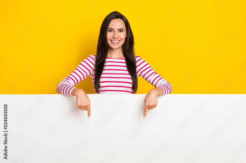 Photo portrait of stunning young lady point white blank wall empty space dressed stylish striped look isolated on yellow color background Photo portrait of stunning young lady point white blank wall empty space dressed stylish striped look isolated on yellow color background