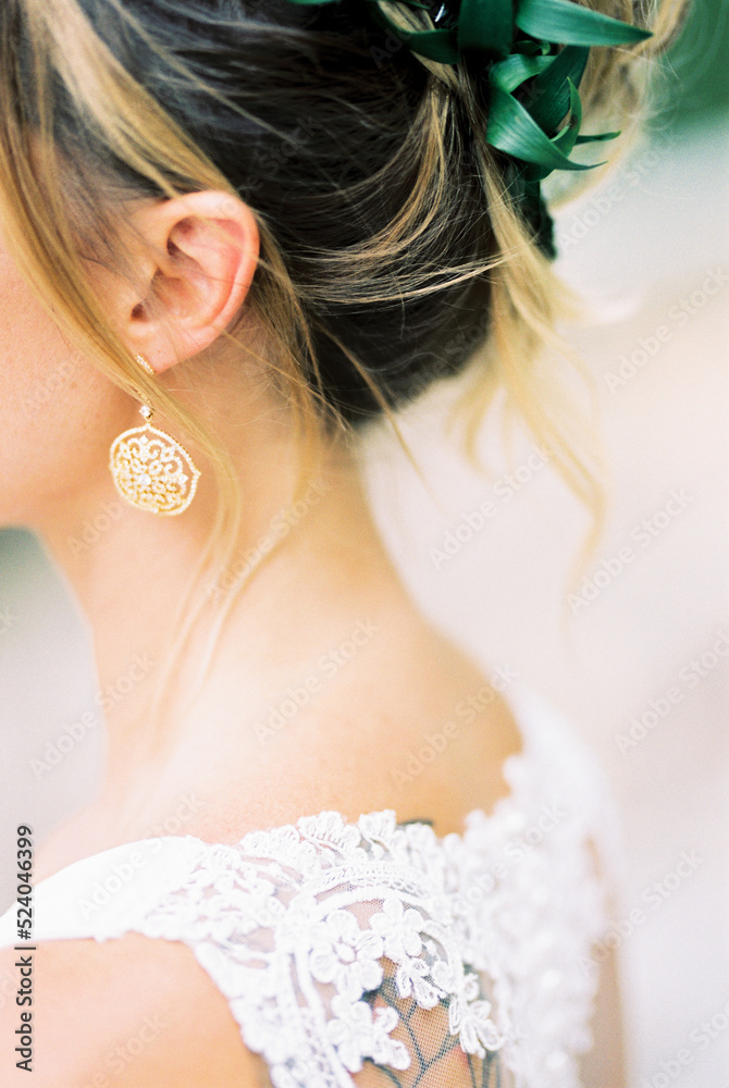Bride in a white dress and gold openwork earrings. Back view. Close-up