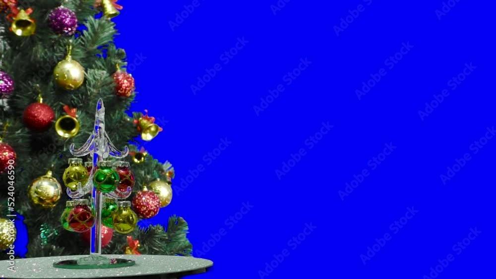 On a blue background, a small Christmas tree rotates near a large Christmas tree decorated with flashing lights and Christmas decorations On a blue background, a small Christmas tree rotates near a large Christmas tree decorated with flashing lights and Christmas decorations