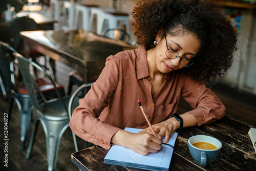 Young black woman making notes in planner book in cafe indoors