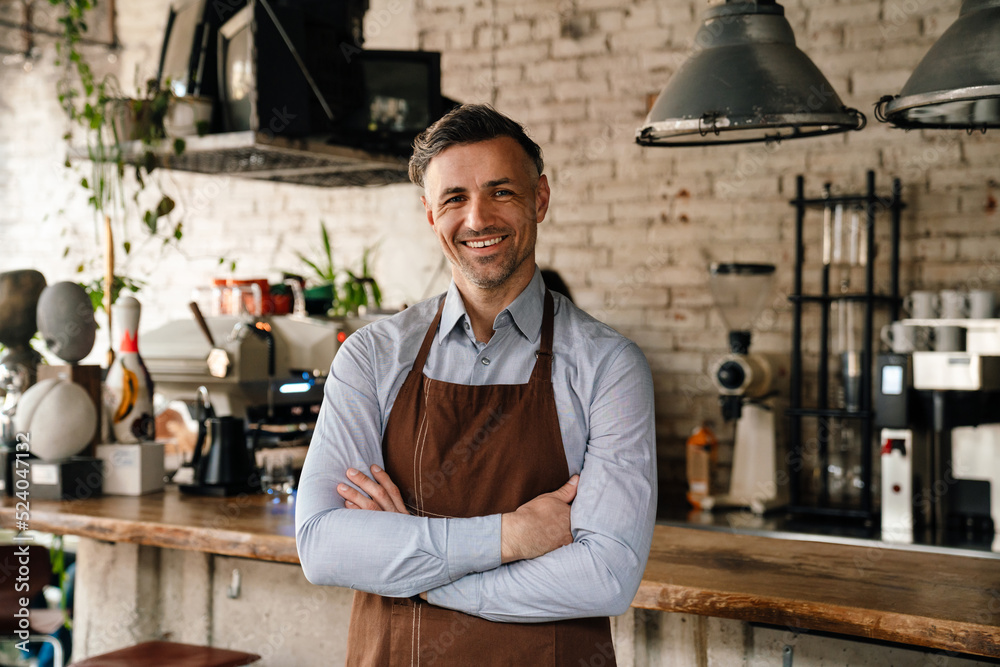 Adult waiter smiling and standing by bar counter while working in cafe