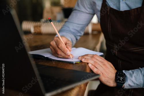 Adult white waiter writing down notes while working on laptop in cafe