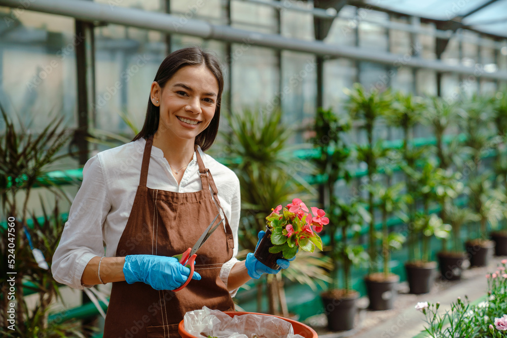 White young woman wearing apron working with plants in greenhouse